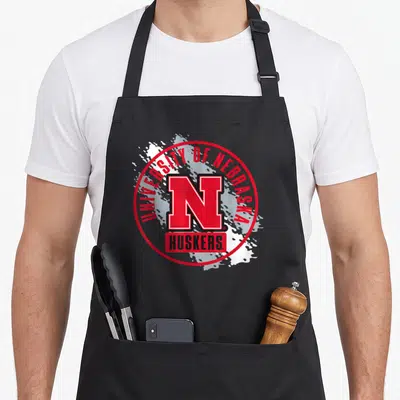 Nebraska paint apron - Red N logo University of Nebraska Huskers white splatter — shown on a black cotton canvas apron against a white background