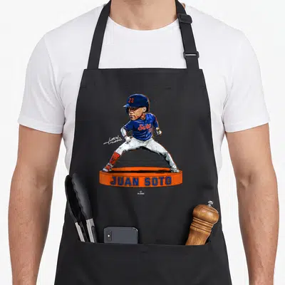 Bobblehead new york apron - Juan Soto caricature on orange podium with blue and orange text — shown on a black cotton canvas apron against a white background