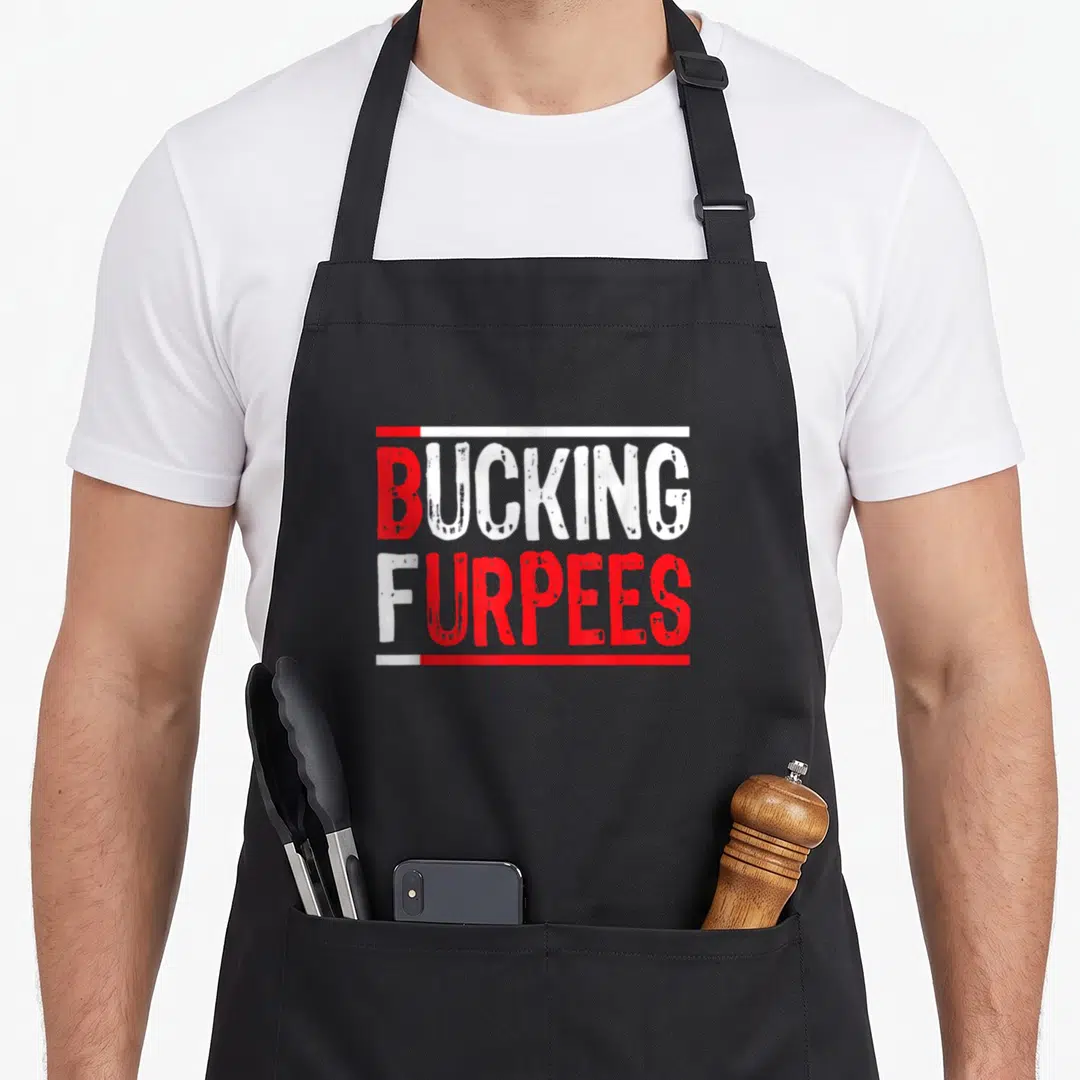 Bucking christmas apron - Red and white stacked text reading BUCKING FURPEES framed by horizontal lines — shown on a black cotton canvas apron against a white background