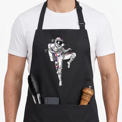 Muay boy astronaut apron - Cartoon astronaut in white suit with red blue stripes performing high kick with rope wraps — shown on a black cotton canvas apron against a white background