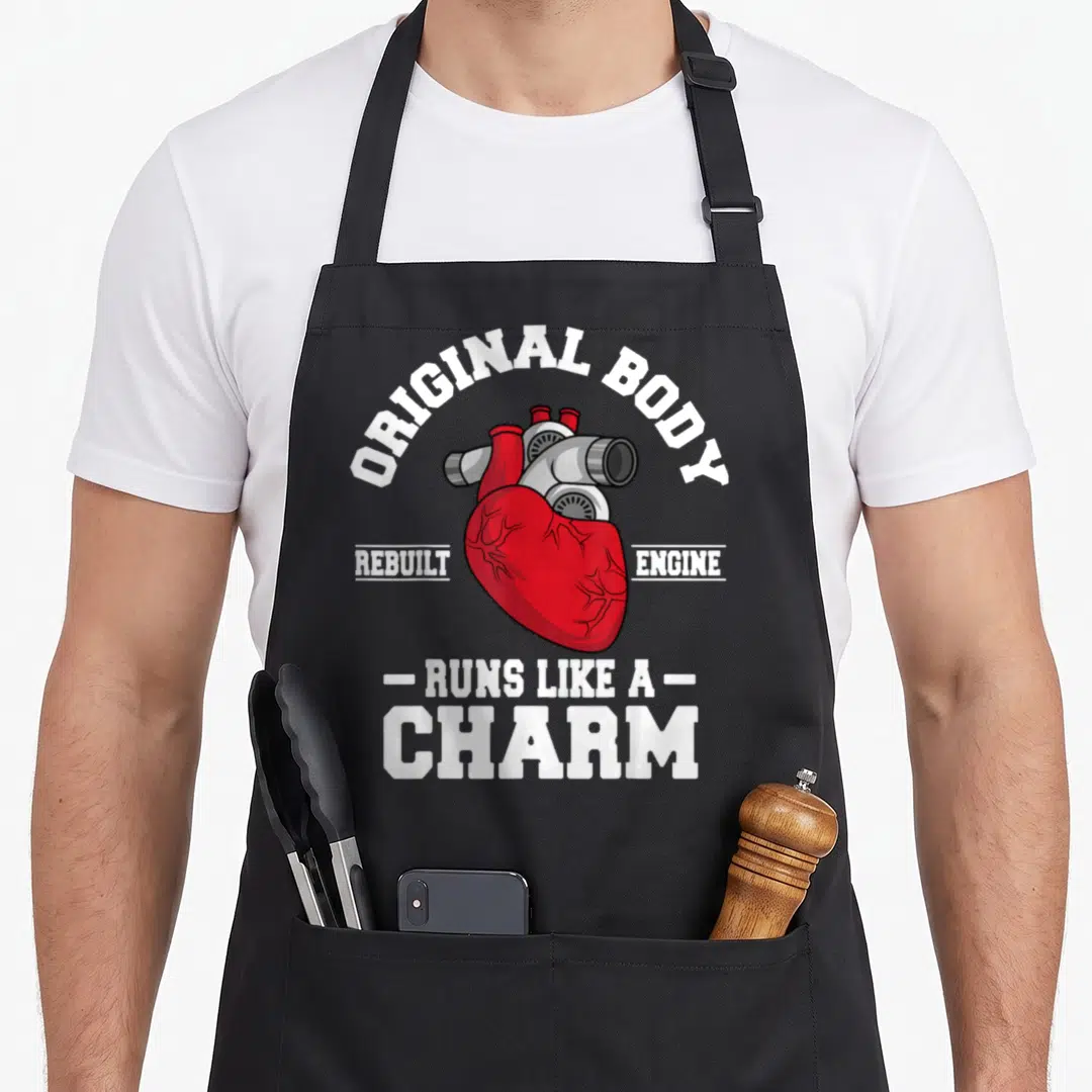 Body open apron - Red heart merged with grey engine pipes and white text reading Original Body Rebuilt Engine Runs Like — shown on a black cotton canvas apron against a white background