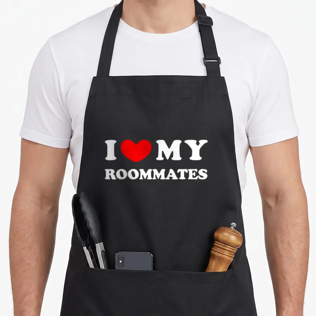 Vintage roommate apron - White text I MY ROOMMATES with red heart symbol on black background — shown on a black cotton canvas apron against a white background