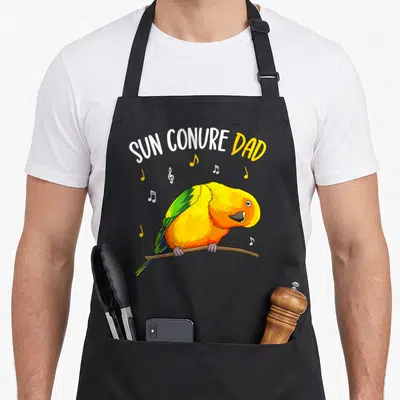 Sun conure bird apron - Cartoon sun conure perched on branch with musical notes and arched text SUN CONURE DAD — shown on a black cotton canvas apron against a white background