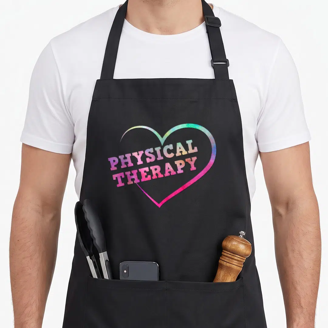 Funny physical my therapy apron - Rainbow heart outline with PHYSICAL THERAPY text in pink blue green yellow — shown on a black cotton canvas apron against a white background