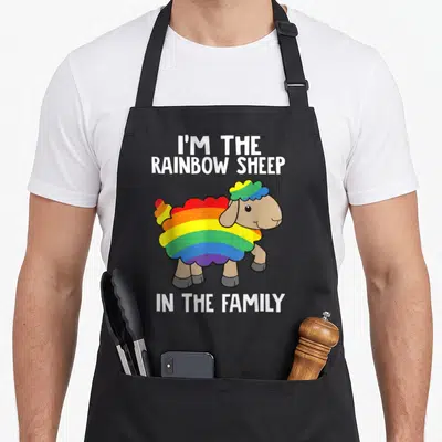 Rainbow sheep apron - Cartoon sheep with red orange yellow green blue purple wool and white text I'M THE RAINBOW SHEEP — shown on a black cotton canvas apron against a white background