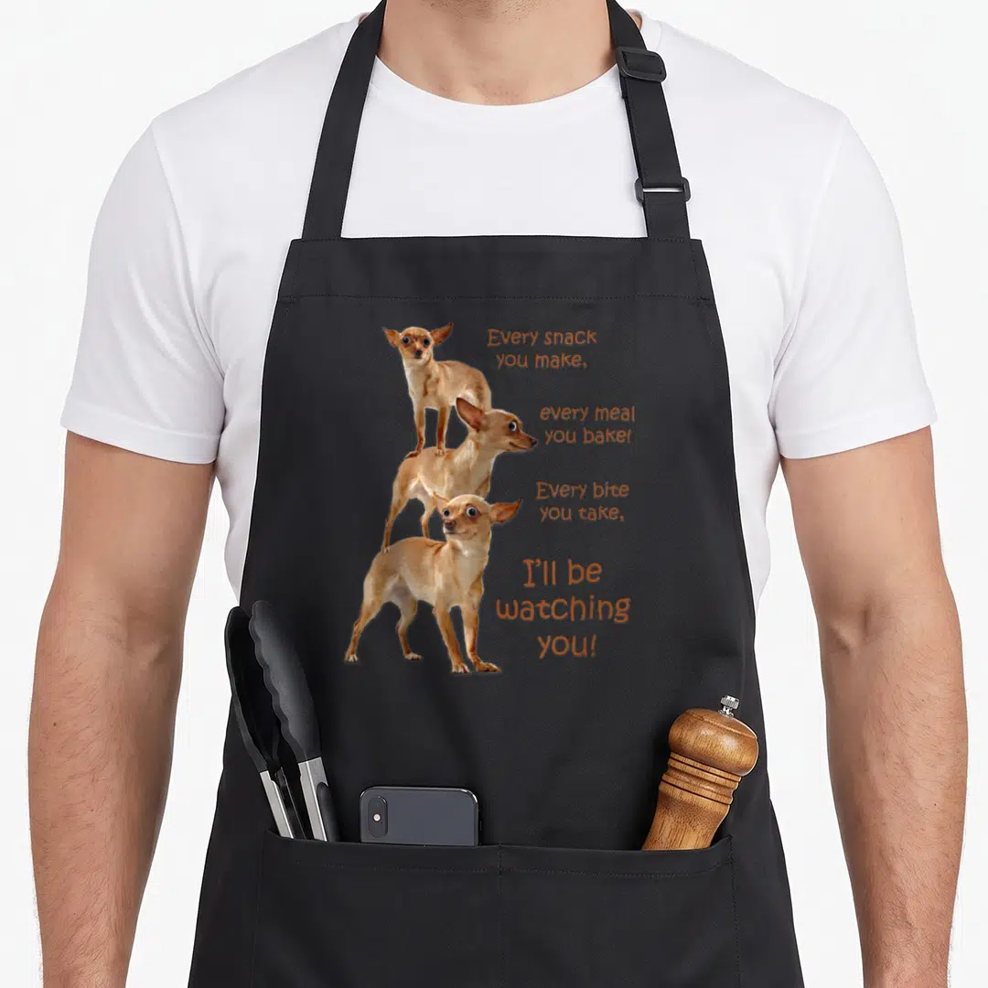 Bite dog apron - Three stacked chihuahuas beside orange text warning about being watched during meals — shown on a black cotton canvas apron against a white background