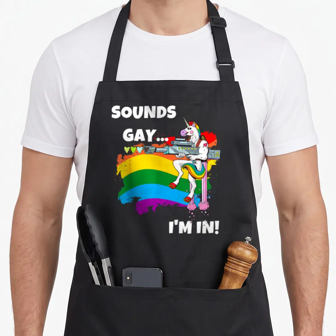 Sound unicorn gay pride apron - White unicorn holding gun on rainbow splatter with text SOUNDS GAY I M — shown on a black cotton canvas apron against a white background