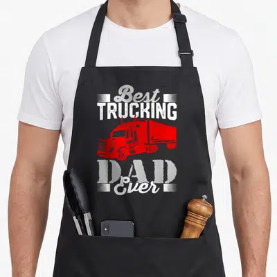 Trucking father day apron - Red semi-truck graphic with stacked Best TRUCKING DAD Ever text in distressed white font — shown on a black cotton canvas apron against a white background