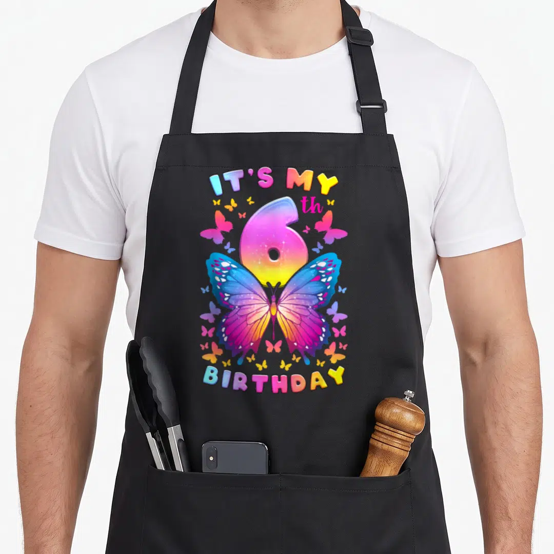 6th birthday butterfly aprons - Rainbow number 6 overlapping a large butterfly with arched IT'S MY BIRTHDAY text — shown on a black cotton canvas apron against a white background