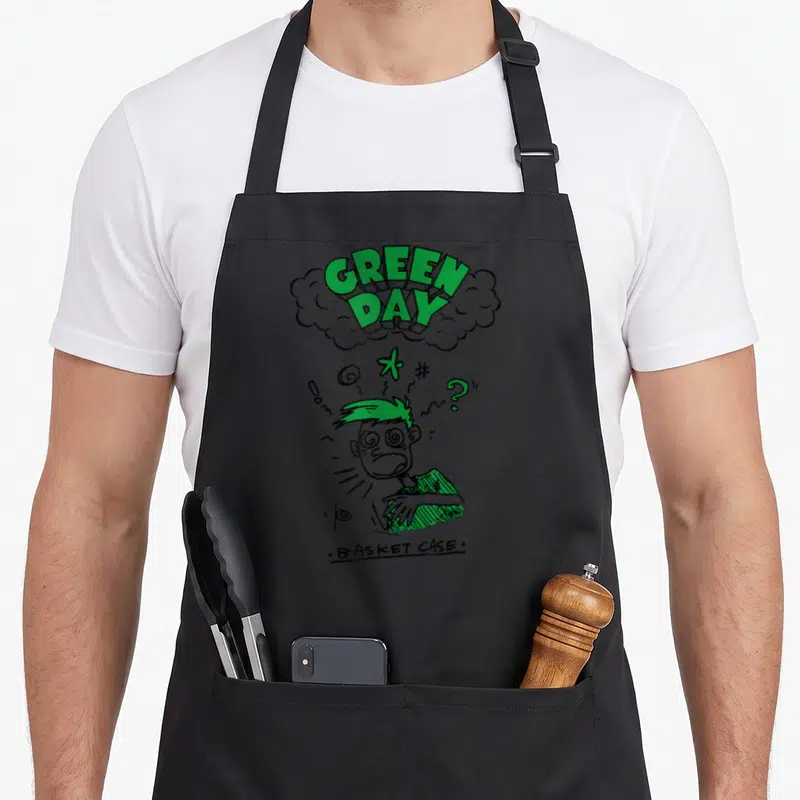 Case basket apron - Cartoon man with spiral eyes under green text cloud reading GREEN DAY BASKET CASE — shown on a black cotton canvas apron against a white background