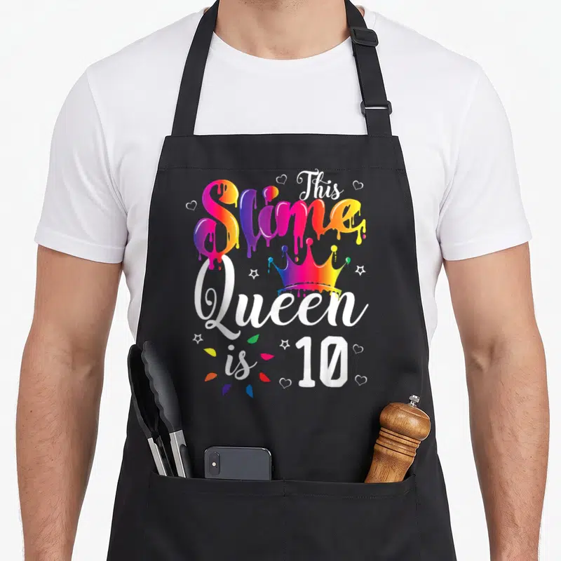 10th queen of baking apron - Rainbow dripping text This Slime Queen is 10 with crown and hearts — shown on a black cotton canvas apron against a white background