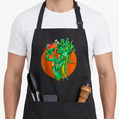 Medusa cartoon apron - Green Medusa figure with snake hair and red flames on an orange circle — shown on a black cotton canvas apron against a white background