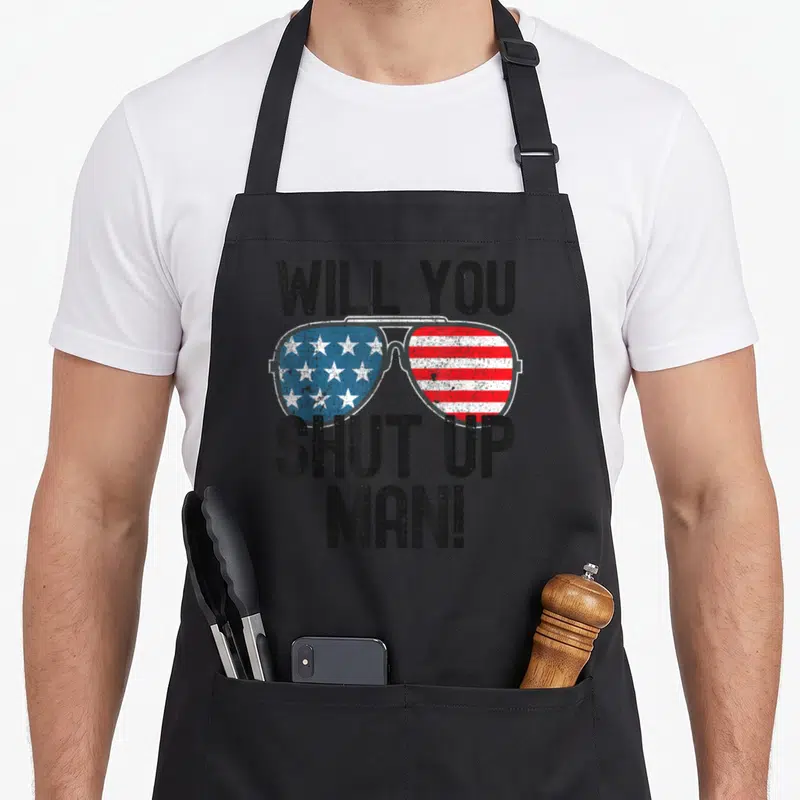 Shut best debate ever apron - Distressed sunglasses with US flag lenses and text Will You Shut Up Man — shown on a black cotton canvas apron against a white background