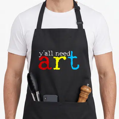 Artist teacher apron - Y'all need art in white red yellow blue stacked typography — shown on a black cotton canvas apron against a white background