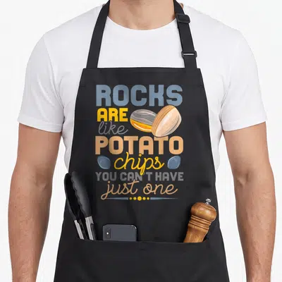 Lapider geologist apron - Rocks are like potato chips text with banded stones and blue pebbles — shown on a black cotton canvas apron against a white background