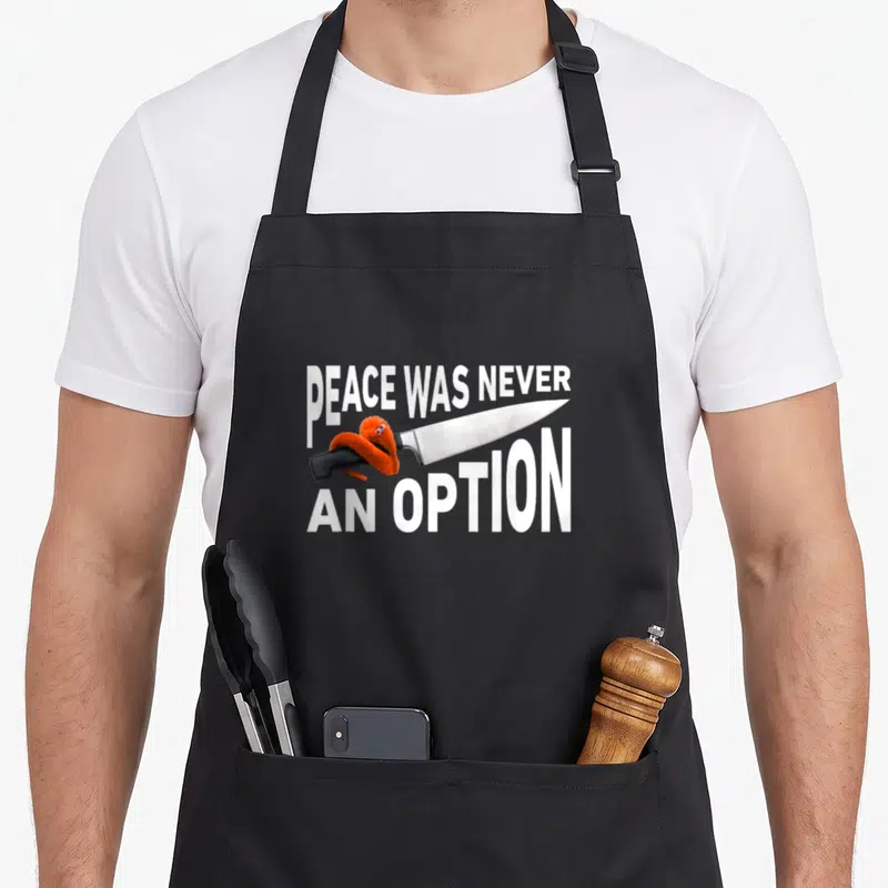 Option meme apron - Silver knife with orange monster and text PEACE WAS NEVER AN OPTION — shown on a black cotton canvas apron against a white background