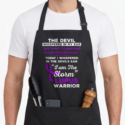 Storm lupus awareness apron - Purple awareness ribbon next to white and purple stacked text reading I am The Storm — shown on a black cotton canvas apron against a white background