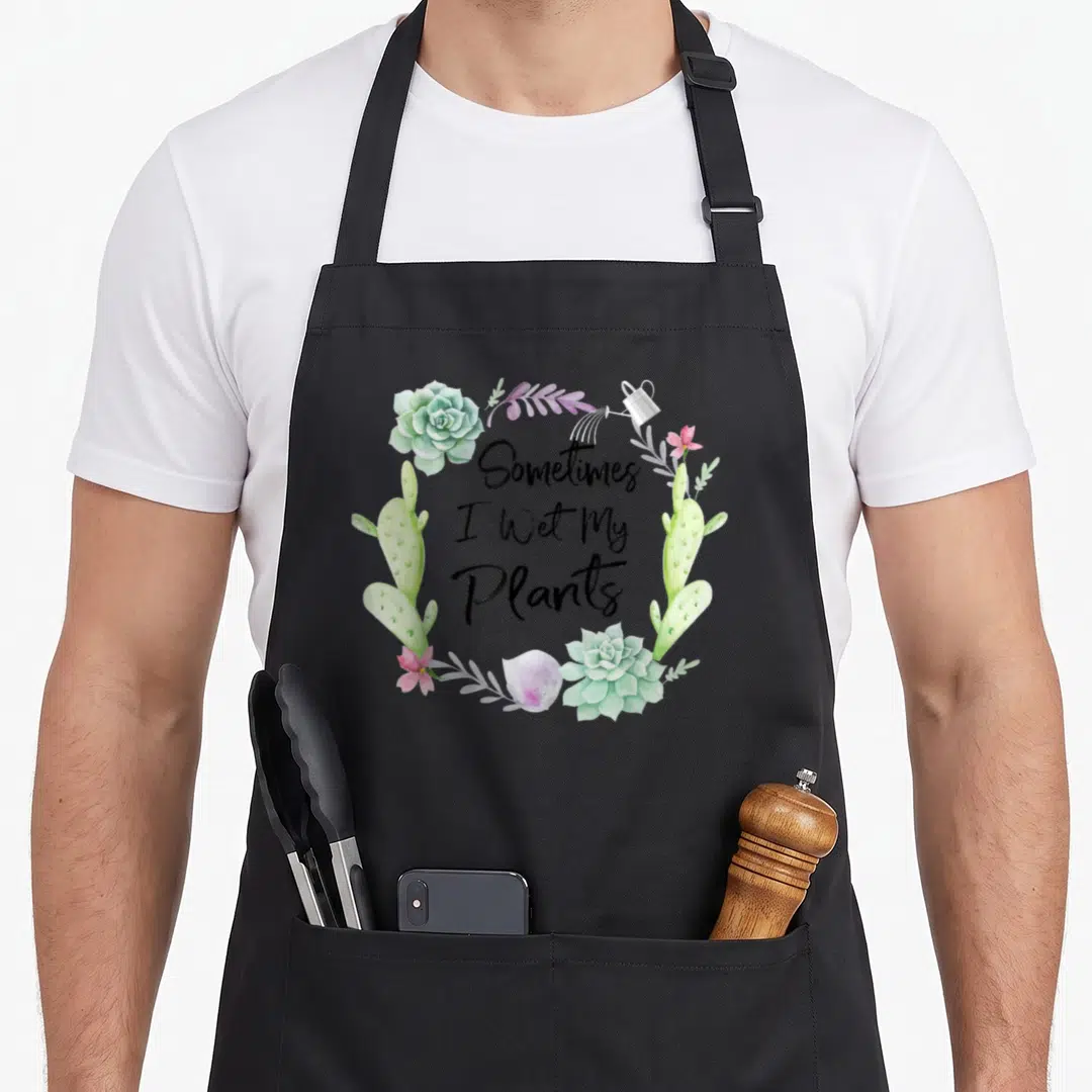 Sometime wet plant apron - Watercolor wreath of succulents cacti and pink flowers surrounding black text — shown on a black cotton canvas apron against a white background