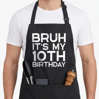 Bruh 10th bday birthday apron - White distressed text reading BRUH IT'S MY 10TH BIRTHDAY stacked vertically — shown on a black cotton canvas apron against a white background