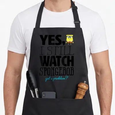 Squarepant problem apron - Stacked text YES I STILL WATCH SPONGEBOB got a problem with small character image — shown on a black cotton canvas apron against a white background