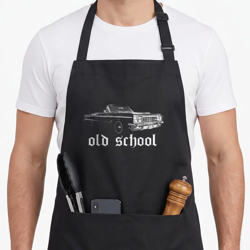 Cholo lowrider girl apron - White distressed lowrider car above old school gothic text — shown on a black cotton canvas apron against a white background