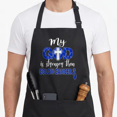 God colon cancer awareness apron - Blue and white text reading my GOD is stronger than COLON CANCER with cross — shown on a black cotton canvas apron against a white background