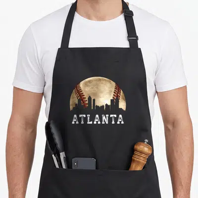 Atlanta skyline baseball apron - Beige baseball with grey skyline silhouette and distressed white ATLANTA text — shown on a black cotton canvas apron against a white background
