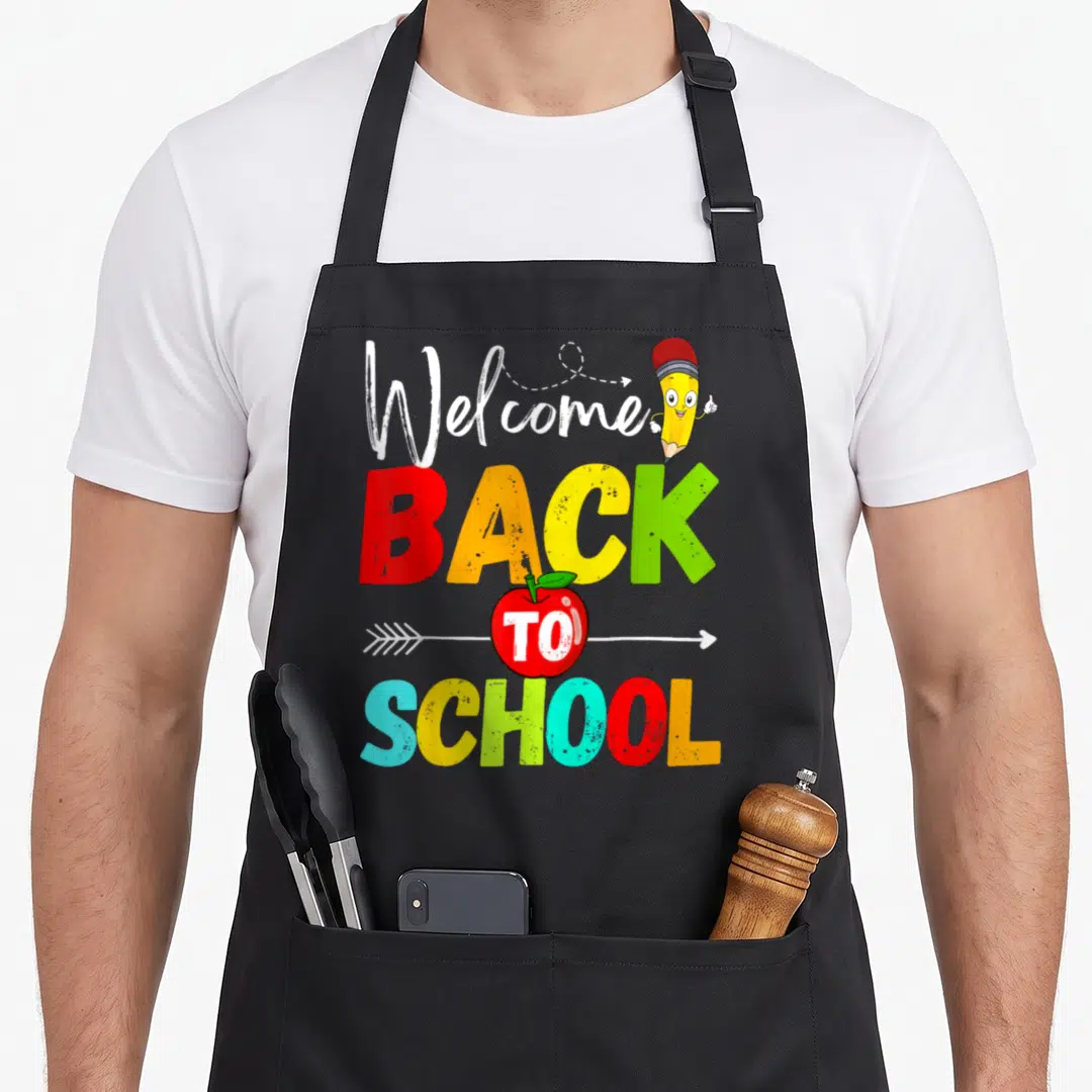 Welcome school art teacher apron - Colorful stacked BACK TO SCHOOL text with cartoon pencil and apple on white arrow — shown on a black cotton canvas apron against a white background