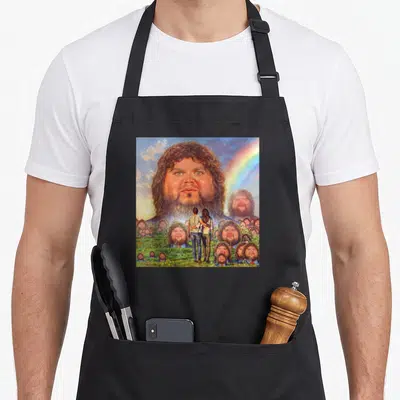 Vance meme apron - Giant bearded man head in sky above couple in field of smaller identical faces with rainbow — shown on a black cotton canvas apron against a white background