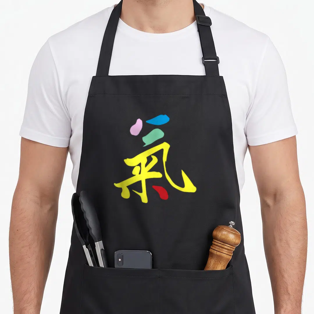 Gong qigong apron - Stylized kanji character made of yellow, blue, pink, green, and red brushstrokes centered on black — shown on a black cotton canvas apron against a white background