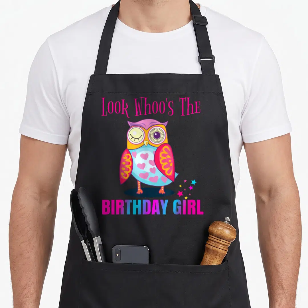 Whoo owl apron - Cartoon owl with Look Whoo's The Birthday Girl text and stars in pink blue yellow purple — shown on a black cotton canvas apron against a white background
