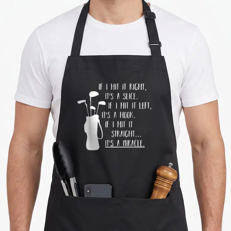 Cute golfing golf apron - White golf bag silhouette next to seven lines of text about slices hooks and miracles — shown on a black cotton canvas apron against a white background