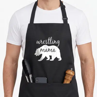 Wrestling mama bear apron - White bear silhouette with wrestling text above and mama inside body — shown on a black cotton canvas apron against a white background