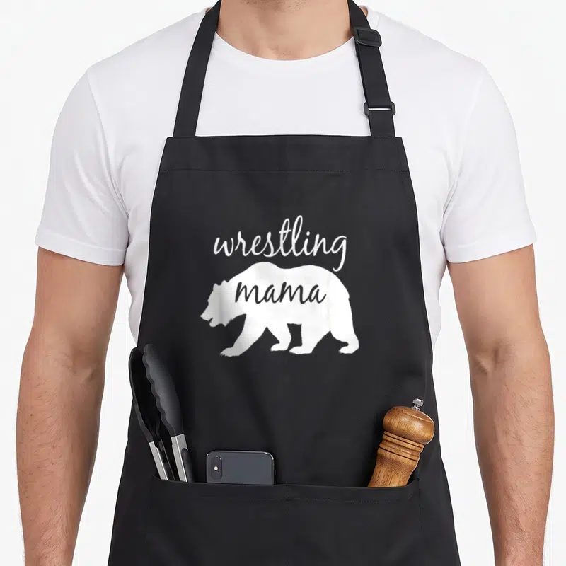 Wrestling mama bear apron - White bear silhouette with wrestling text above and mama inside body — shown on a black cotton canvas apron against a white background