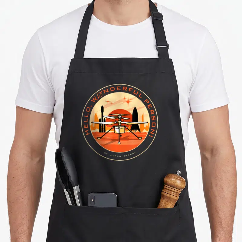 Wonderful mars apron - Retro circular drone design with Hello Wonderful Person text and red sun — shown on a black cotton canvas apron against a white background