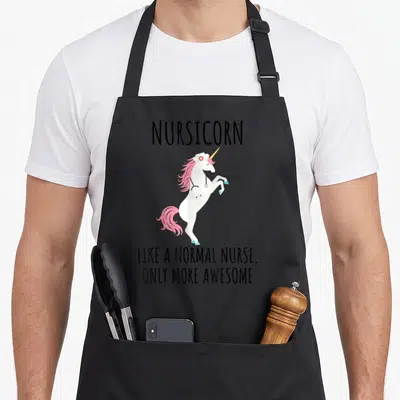Normal nurse apron - Cartoon white unicorn with pink mane wearing a nurse cap and stethoscope with black text above — shown on a black cotton canvas apron against a white background