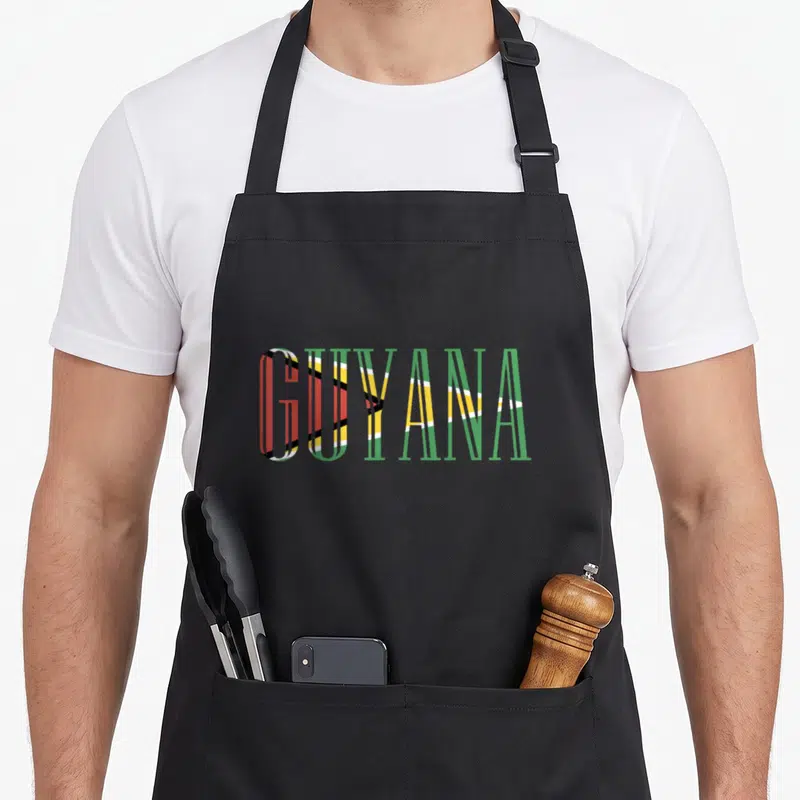 Flag guyanese apron - GUYANA text filled with green yellow red white and black flag stripes — shown on a black cotton canvas apron against a white background