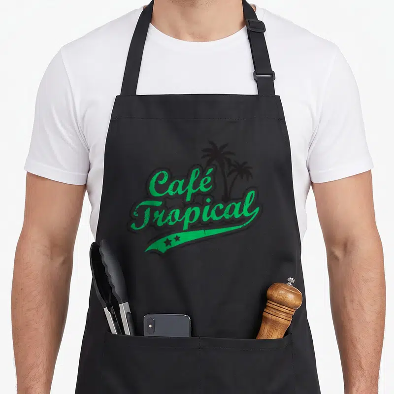 Tropical cafe apron - Retro green Café Tropical text with two black palm trees and a curved banner below — shown on a black cotton canvas apron against a white background