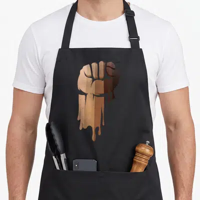 Drippin african apron - Brown and tan cartoon clenched fist with dripping effect — shown on a black cotton canvas apron against a white background