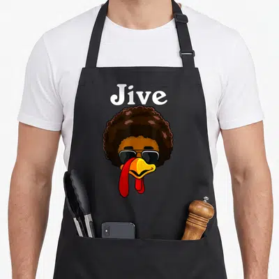 Turkey family thanksgiving day aprons - Cartoon chicken head with brown afro and sunglasses under white Jive text — shown on a black cotton canvas apron against a white background
