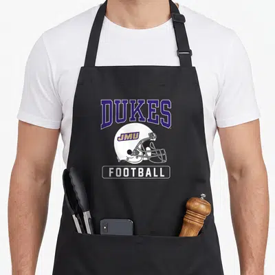 Jame football apron - White football helmet with JMU logo under DUKES text and FOOTBALL label — shown on a black cotton canvas apron against a white background
