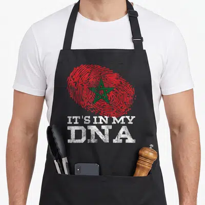 Dna arab apron - Red fingerprint with green star and white IT'S IN MY DNA text — shown on a black cotton canvas apron against a white background