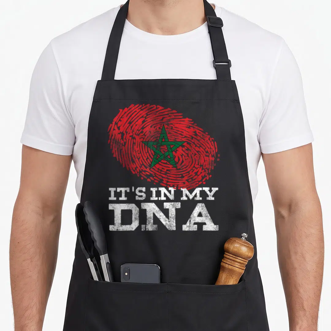 Dna arab apron - Red fingerprint with green star and white IT'S IN MY DNA text — shown on a black cotton canvas apron against a white background