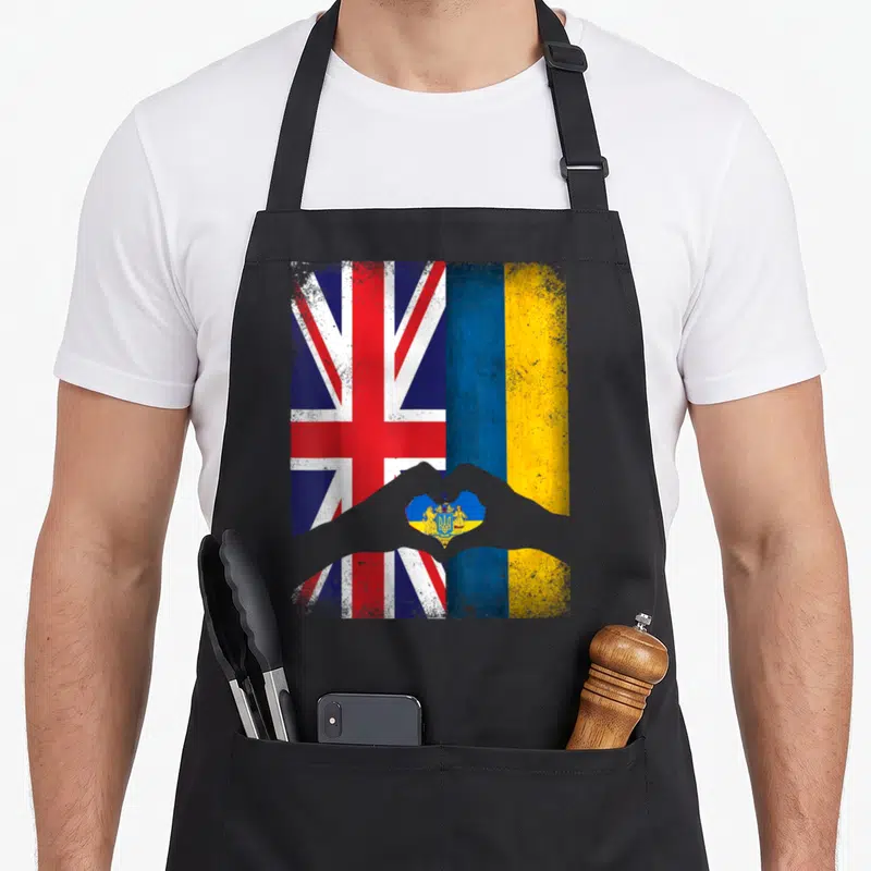 Ukrainian uk aprons - Two flags side-by-side with grey hands forming a heart containing a coat of arms in distressed — shown on a black cotton canvas apron against a white background