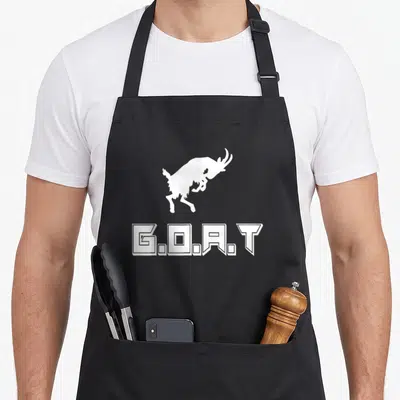 Funny greatest apron - White jumping goat silhouette above G.O.A.T block text — shown on a black cotton canvas apron against a white background