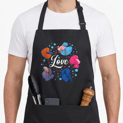 Pet fish apron - Five betta fish in blue pink orange red surrounding white Love text with hearts and bubbles — shown on a black cotton canvas apron against a white background
