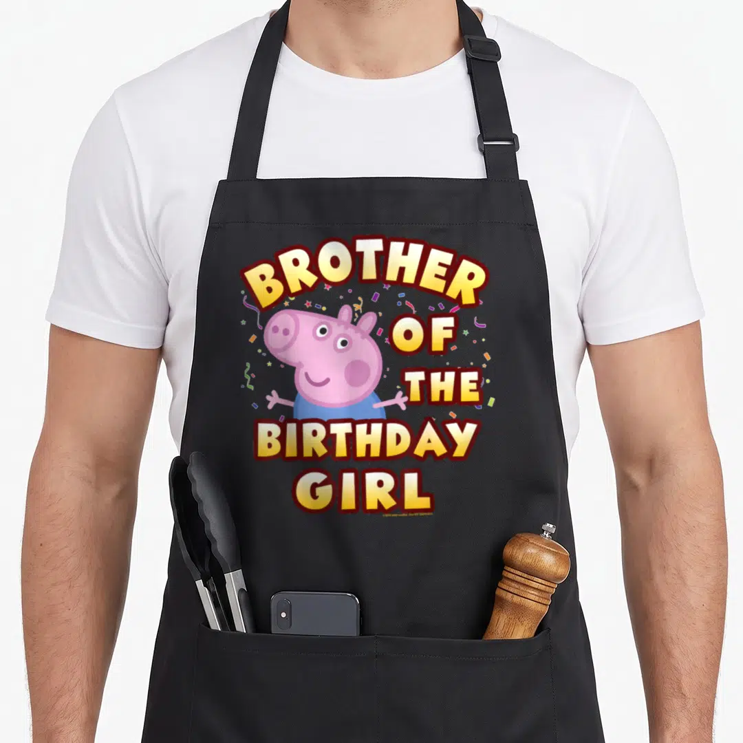 Cool brother birthday apron - Pink cartoon pig in blue shirt with yellow text and multicolored confetti scattered around — shown on a black cotton canvas apron against a white background