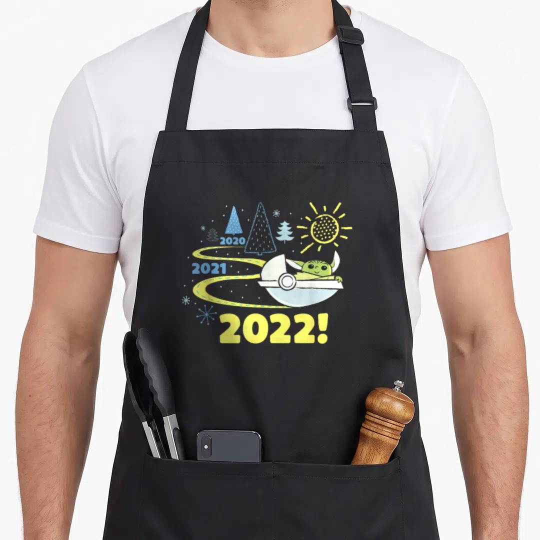 Funny new years eve apron - Grogu in a white pod racer on a yellow road with years 2020 2021 2022 and trees — shown on a black cotton canvas apron against a white background