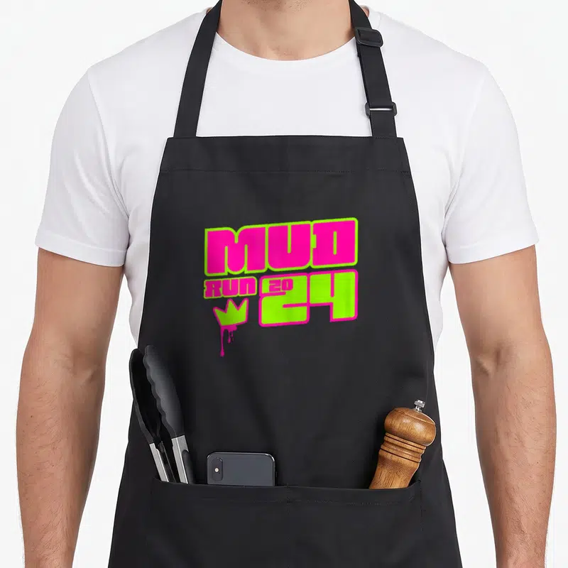 Muddy princess apron - Pink and lime green MUD RUN 2024 text with dripping crown graphic — shown on a black cotton canvas apron against a white background