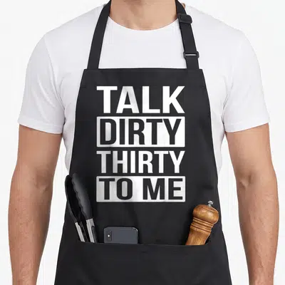 Talk funny dirty aprons - White stacked text TALK DIRTY THIRTY TO ME on black background — shown on a black cotton canvas apron against a white background